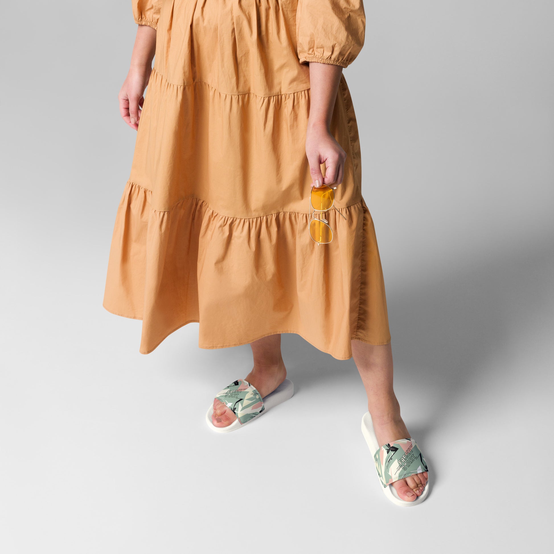 Person wearing a mustard yellow dress with white sandals on a gray background