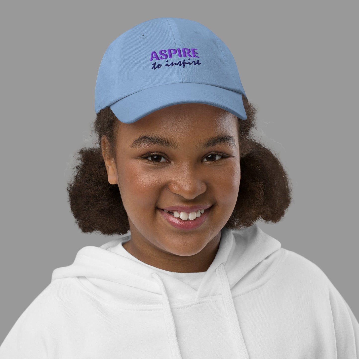 Child wearing a blue cap with 'ASPIRE to inspire' text on a white background