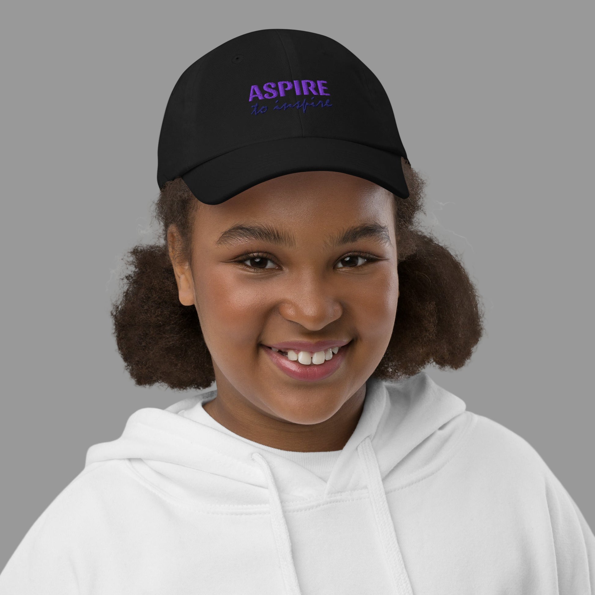 Young girl wearing a black cap with 'ASPIRE' text on a white background
