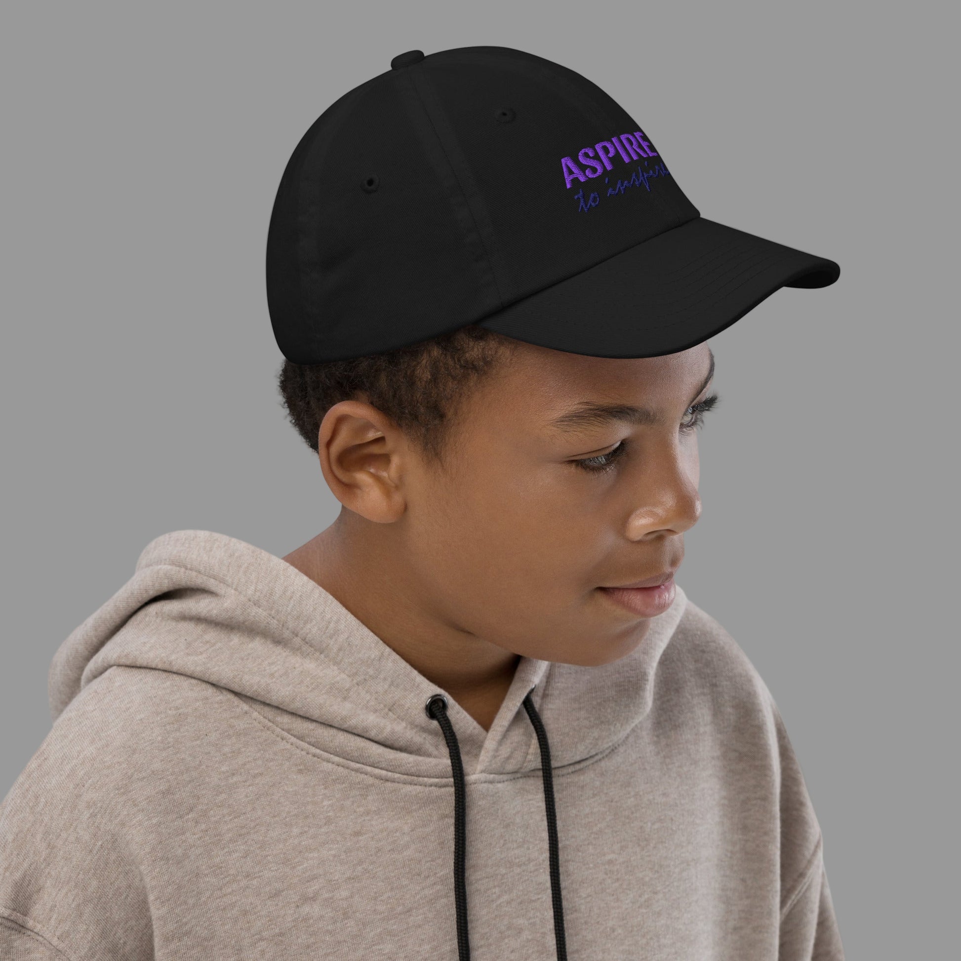 Child wearing a black cap with 'ASPIRE' text on a plain background