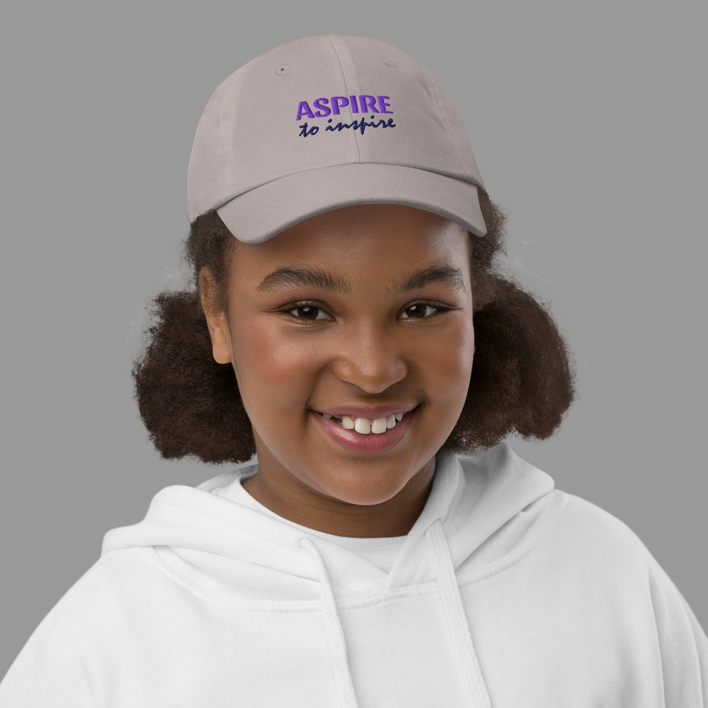 Child wearing a cap with 'ASPIRE to inspire' text on a white background