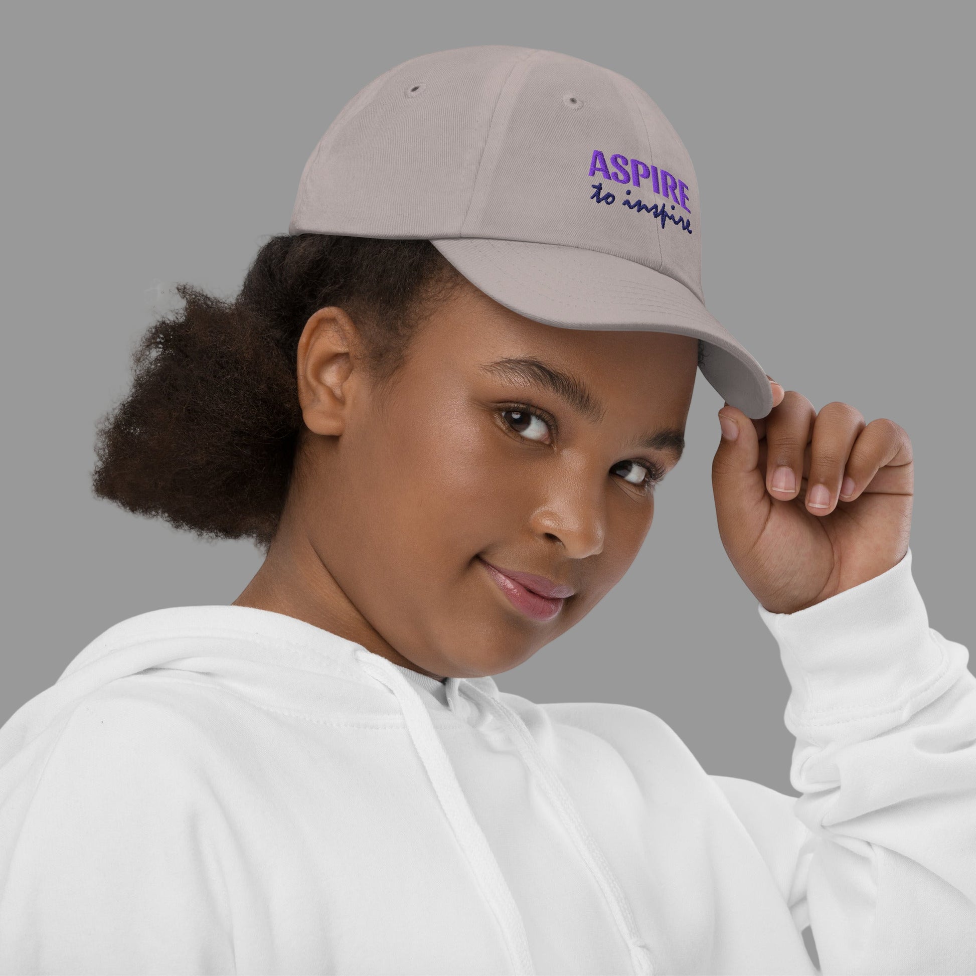 Person wearing a beige cap with 'ASPIRE to inspire' text on a white background
