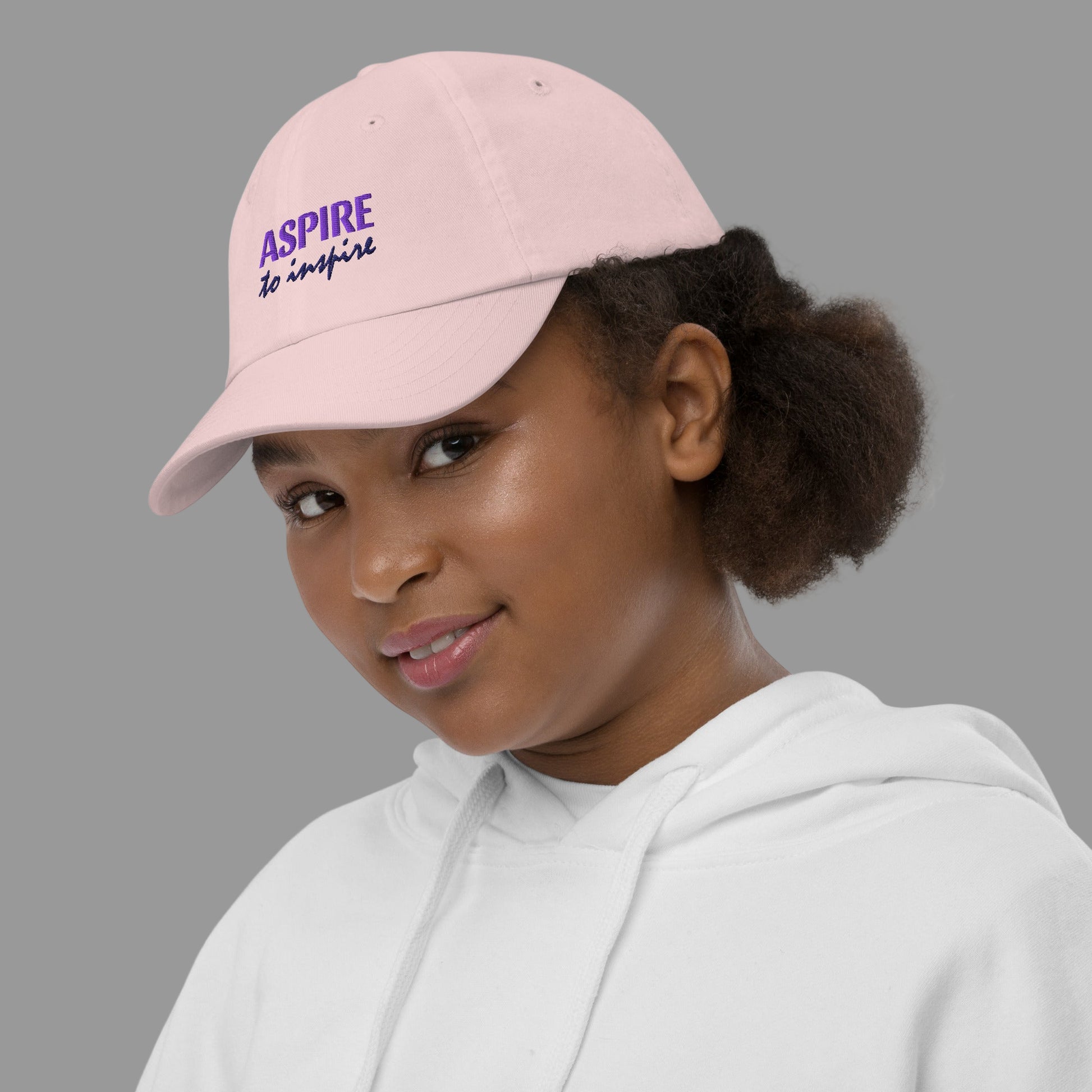 Person wearing a pink cap with 'Aspire' text and a white hoodie on a white background