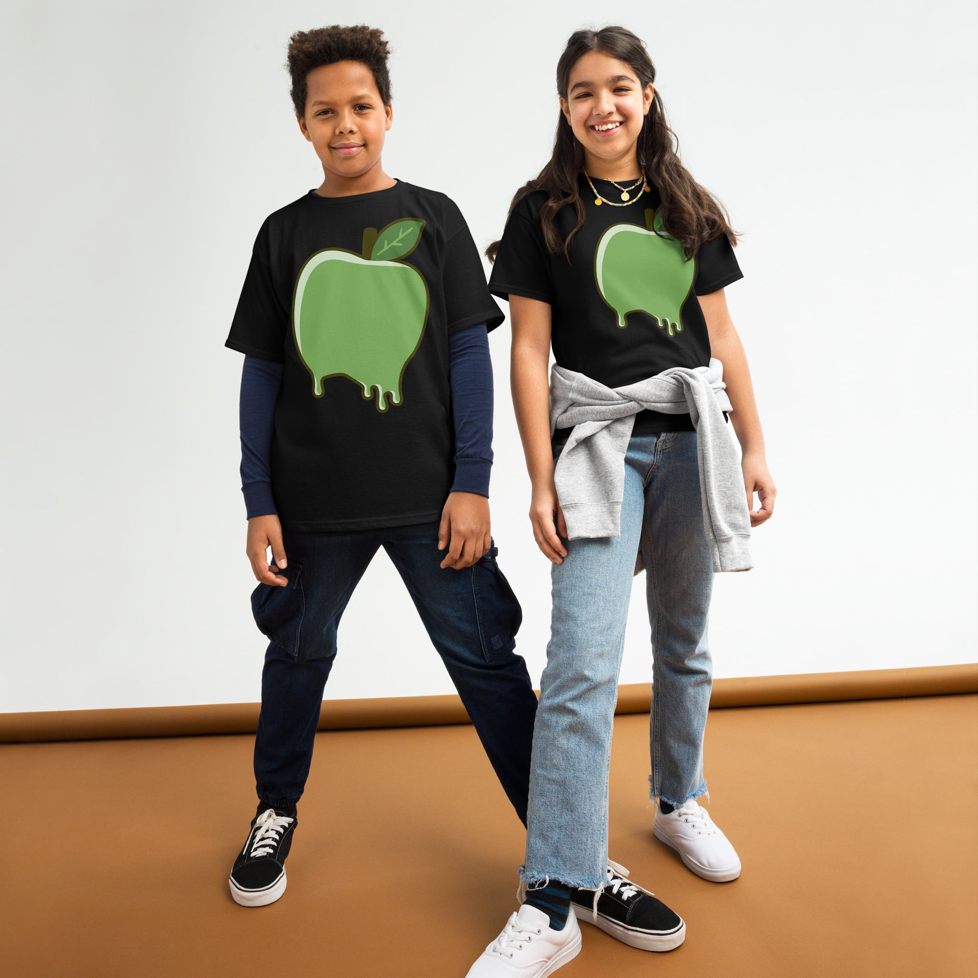 Two children wearing black t-shirts with green apple designs on a white background.