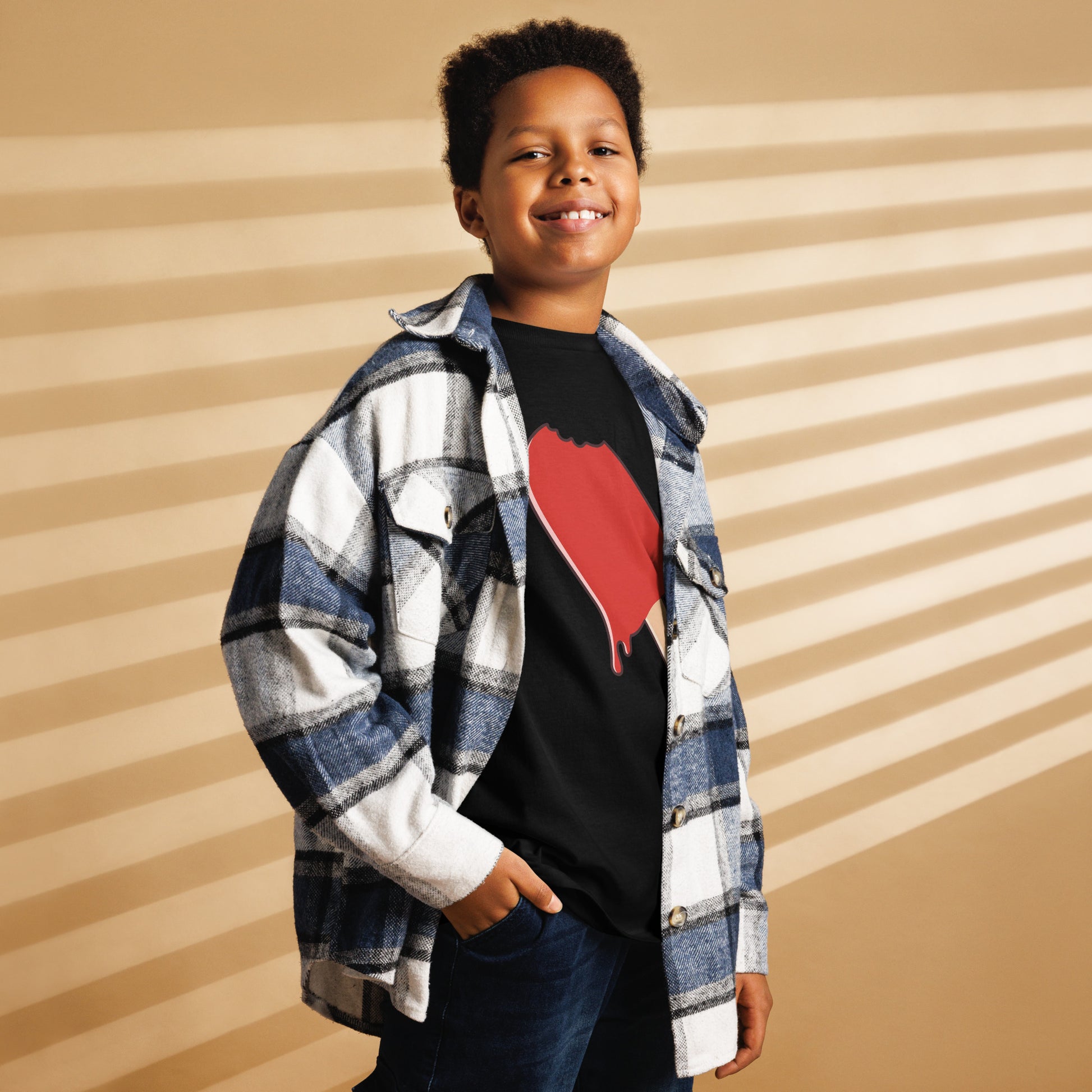 Child wearing a plaid shirt over a black t-shirt with a red heart design, standing against a striped background.