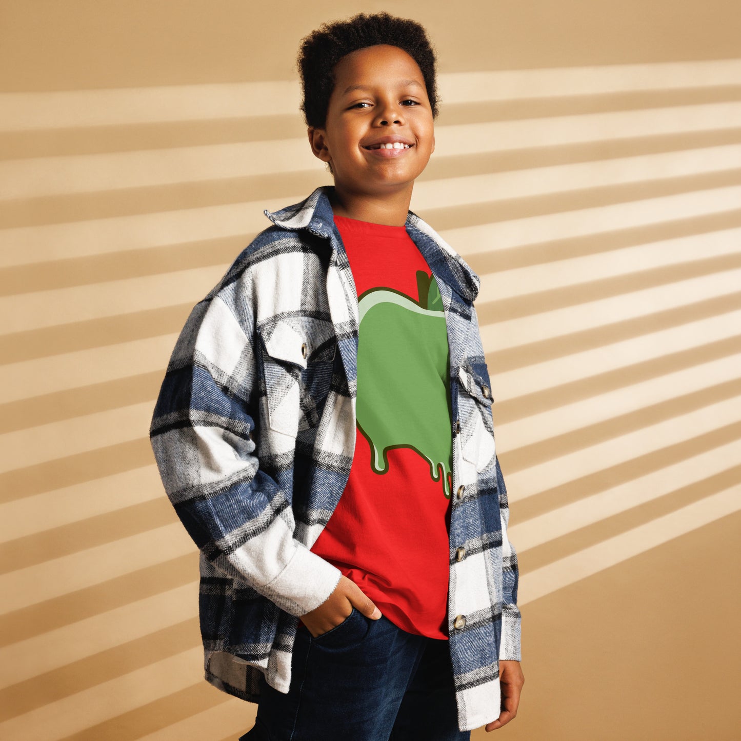 Child wearing a red shirt with a green graphic and a plaid jacket against a striped background