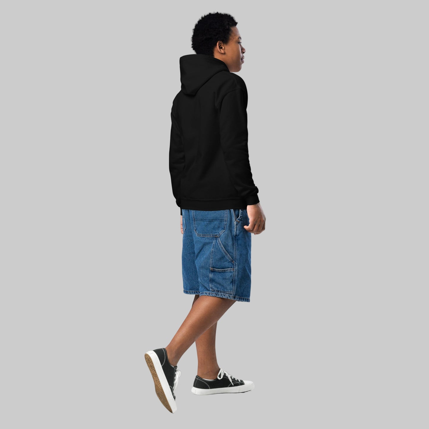 Person wearing a black hoodie and blue shorts on a white background