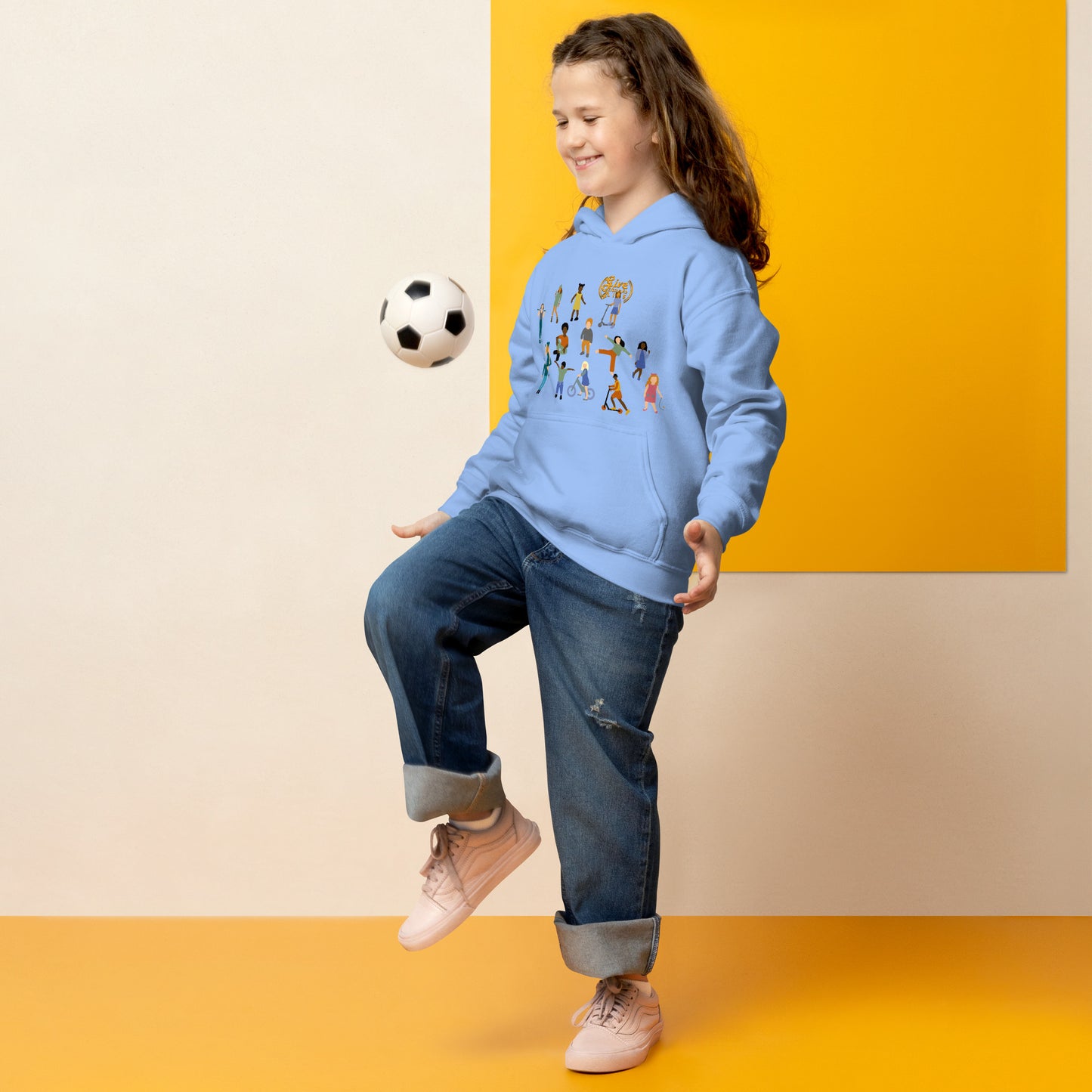 Child wearing a blue hoodie with cartoon characters, kicking a soccer ball against a yellow and beige background