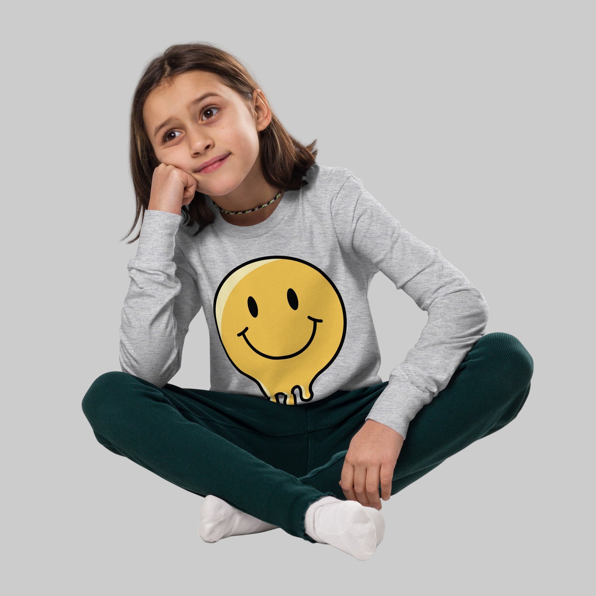 Young girl wearing a gray long-sleeve shirt with a yellow smiley face design on a white background