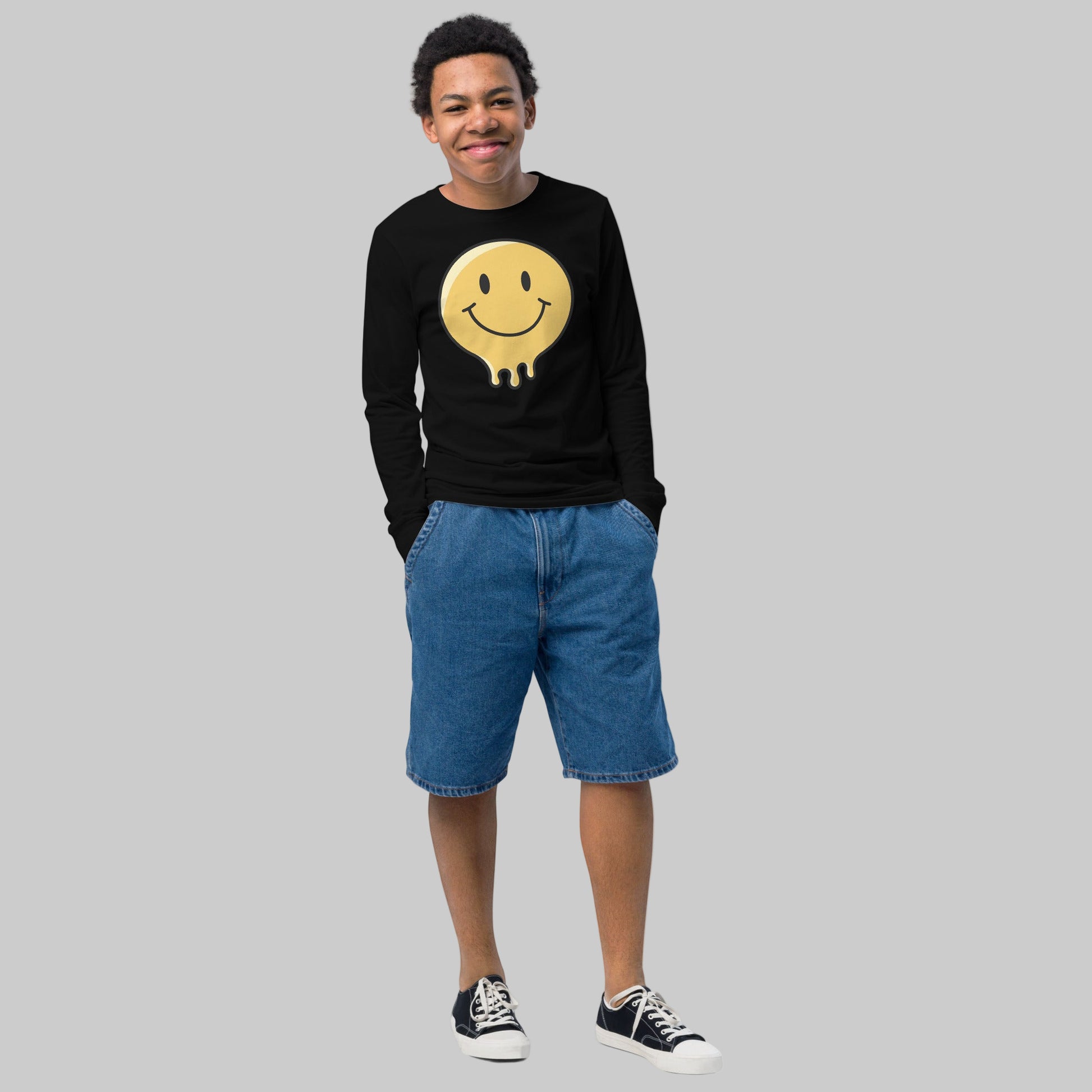 Person wearing a black sweatshirt with a smiley face graphic and blue shorts on a white background