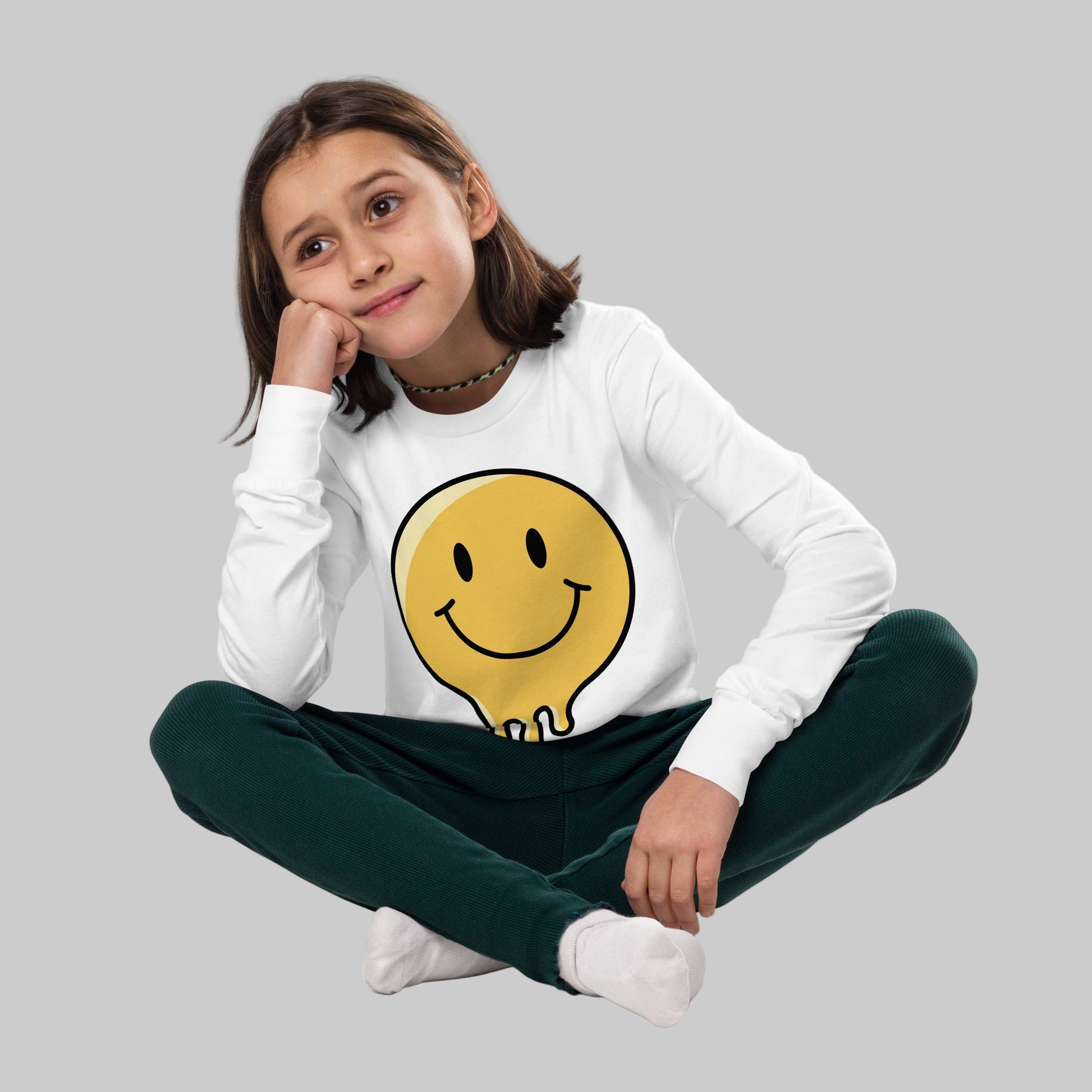 Young girl wearing a white long-sleeve shirt with a yellow smiley face design on a white background