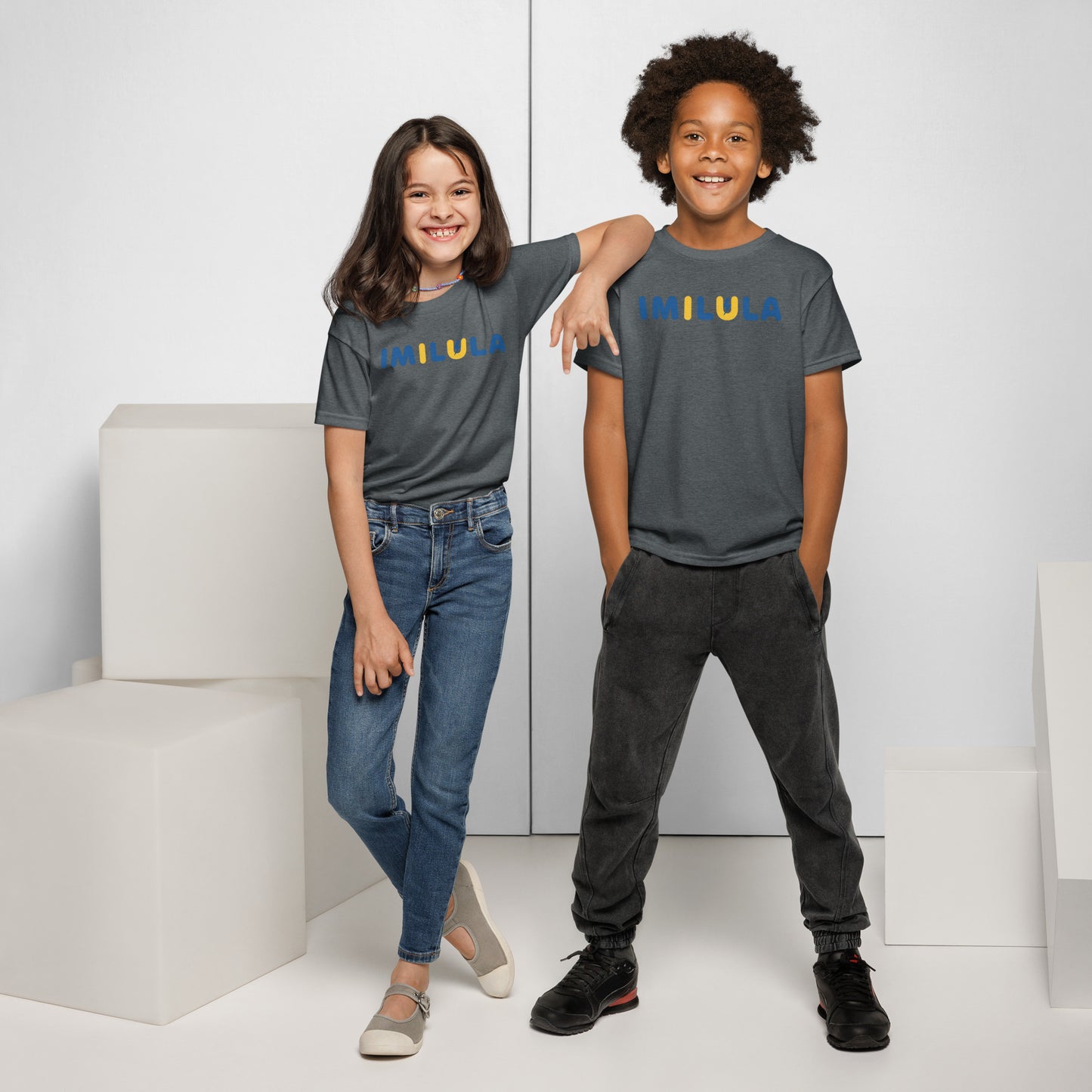 Two children wearing matching gray t-shirts and jeans standing in a minimalistic setting.
